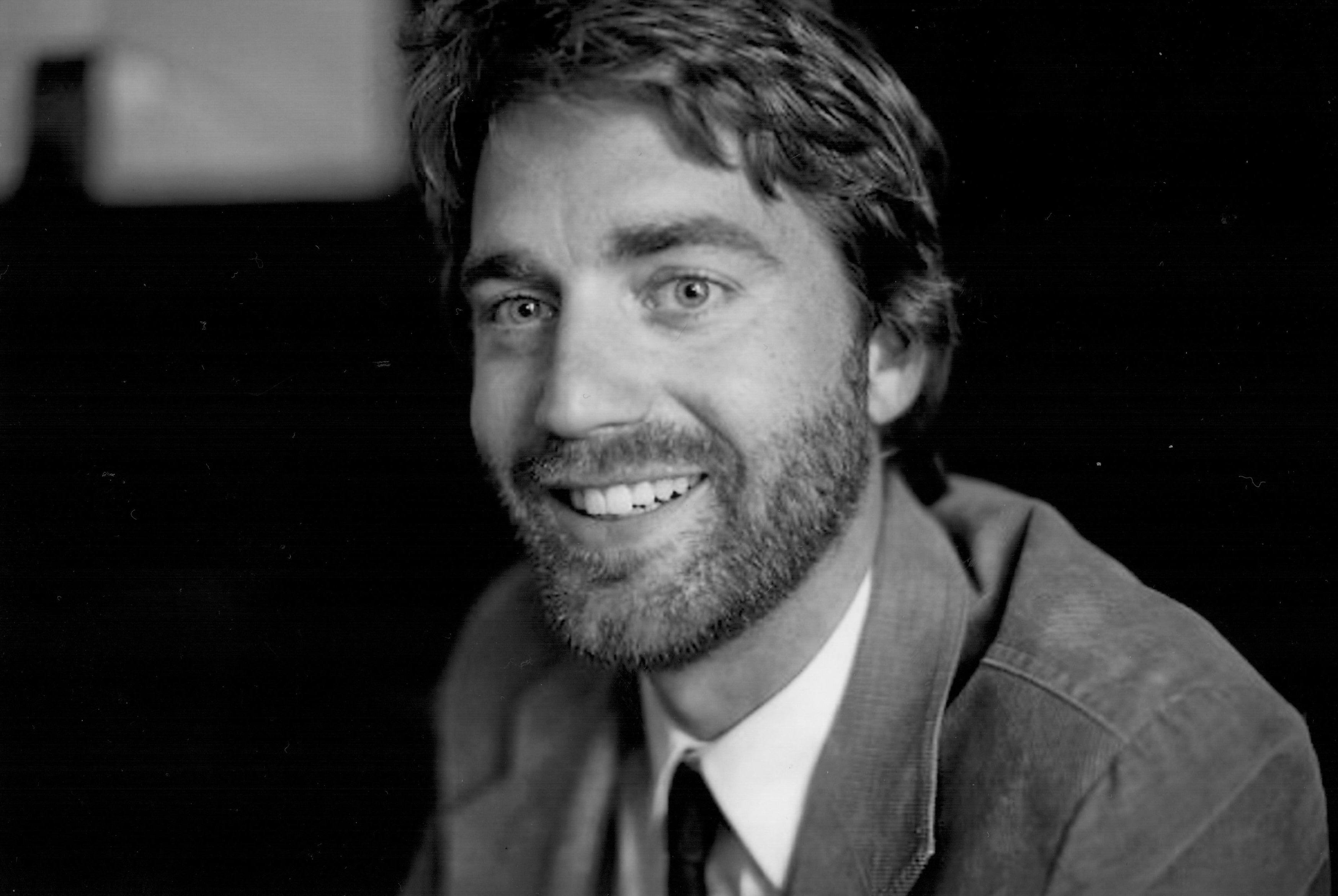 black and white headshot of man with a beard in a jacket, shirt, and tie