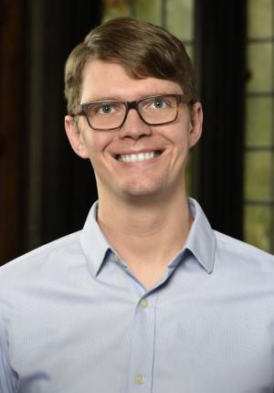 Man in blue shirt with glasses standing in front of a green and black wall