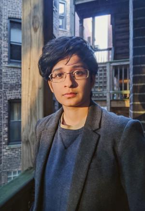 A person in a blazer with short hair and glasses standing on a balcony