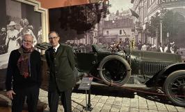 two men standing in front of a early 20th c car in a museum