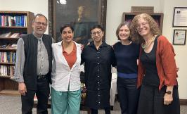 five people standing in front of a large portrait and bookshelves
