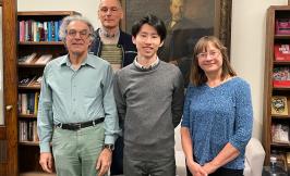 four people standing in front of a large portrait and bookshelves