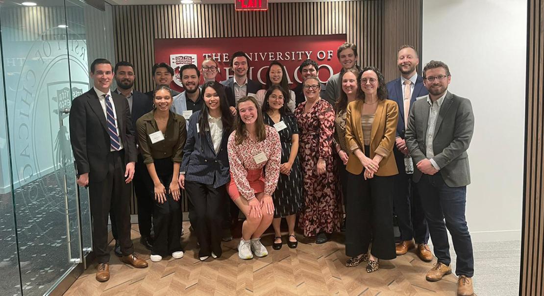 A group of students and alumni standing in front of the logo of the University of Chicago.