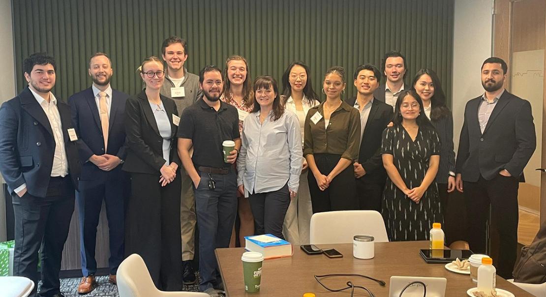 A group of students standing with an alumnus in a conference room.