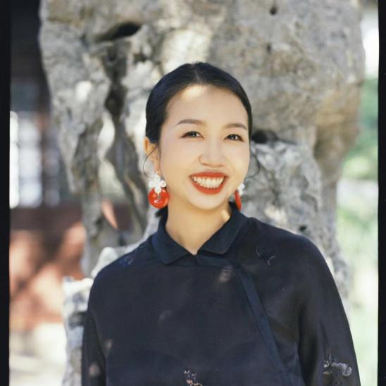 Woman in black shirt wearing red earrings standing in front of a tree