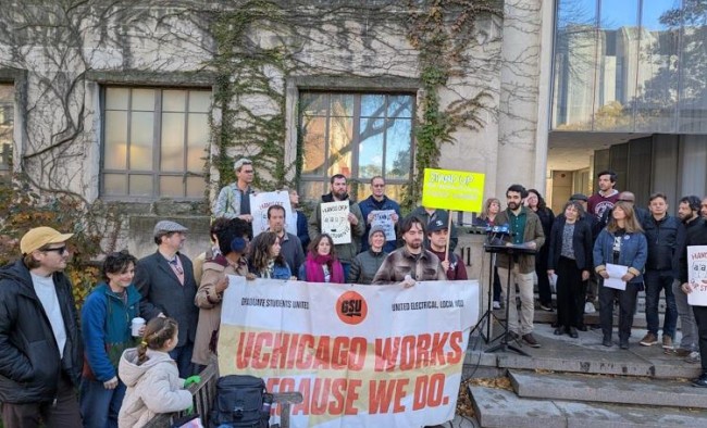 Speakers at a union rally displaying a sign that reads "UChicago Works Because We Do."